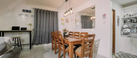 A dining area with a wooden table and chairs, a laptop on a desk, and a grey curtain.