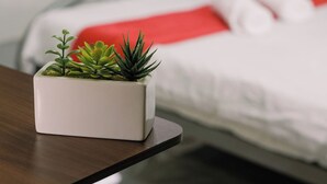 Ein Schlafzimmer mit einem Bett, einem Nachttisch mit Topfpflanze und einem Fenster mit Jalousien.