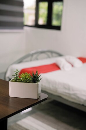 Una camera da letto con un letto, un comodino con una pianta in vaso e una finestra con persiane.