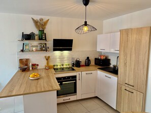 Eine moderne Küche mit weißen Schränken, einer Holz Arbeitsplatte, einem eingebauten Backofen und einer Pendelleuchte.