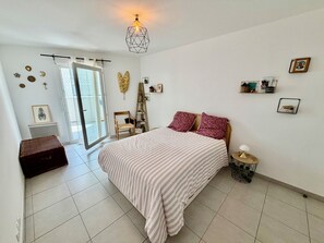 Quarto com cama, poltrona, mesa de cabeceira, luminária e janela.