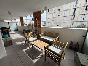 Terraço no telhado com mesa e cadeiras de madeira, um banco e um pequeno móvel decorativo.