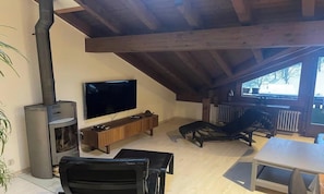 Ein gemütliches Zimmer mit Fernseher, Holzmöbeln, Kamin und Blick ins Freie.