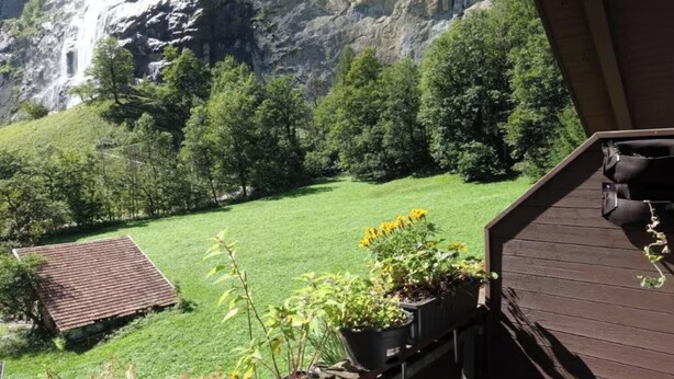 A view of a green lawn with a small building and a waterfall in the background. - STUNNING 3-BEDROOM APARTMENT FACING STAUBBACH FALLS (Lauterbrunnen)