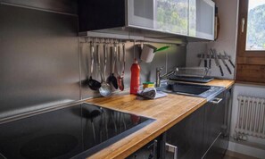 A modern kitchen with a wooden countertop, stainless steel appliances, and hanging utensils. - STUNNING 3-BEDROOM APARTMENT FACING STAUBBACH FALLS (Lauterbrunnen)