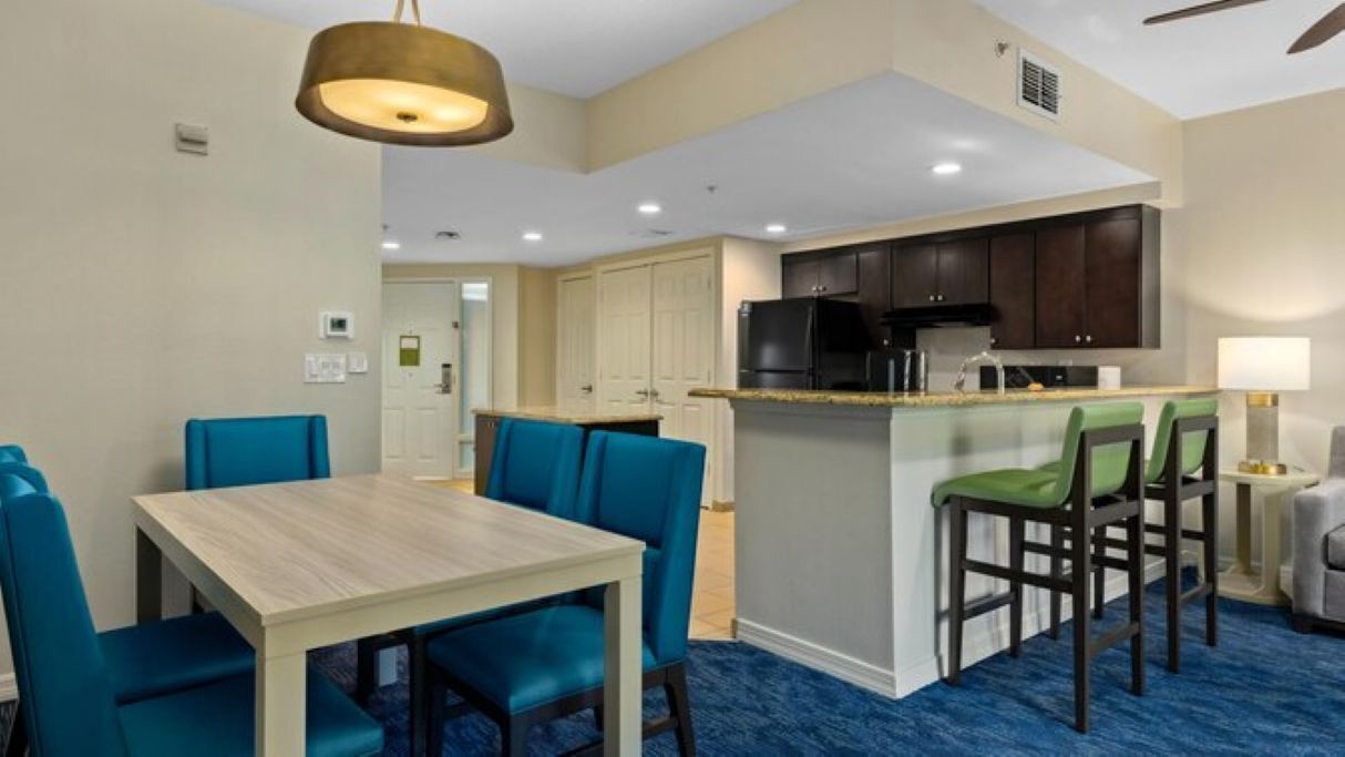 A hotel room with a dining area, kitchenette, and a blue carpet.