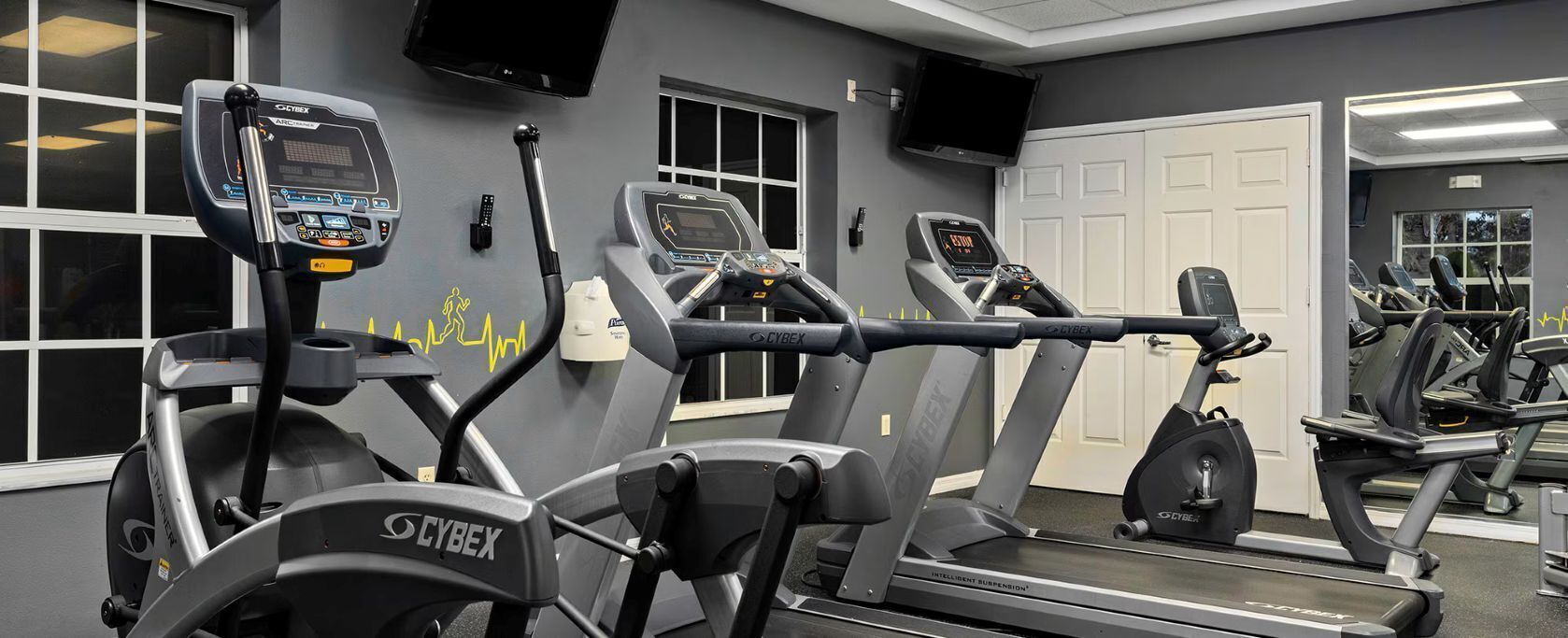 Un gimnasio con cintas de correr, bicicletas estáticas y un espejo grande.