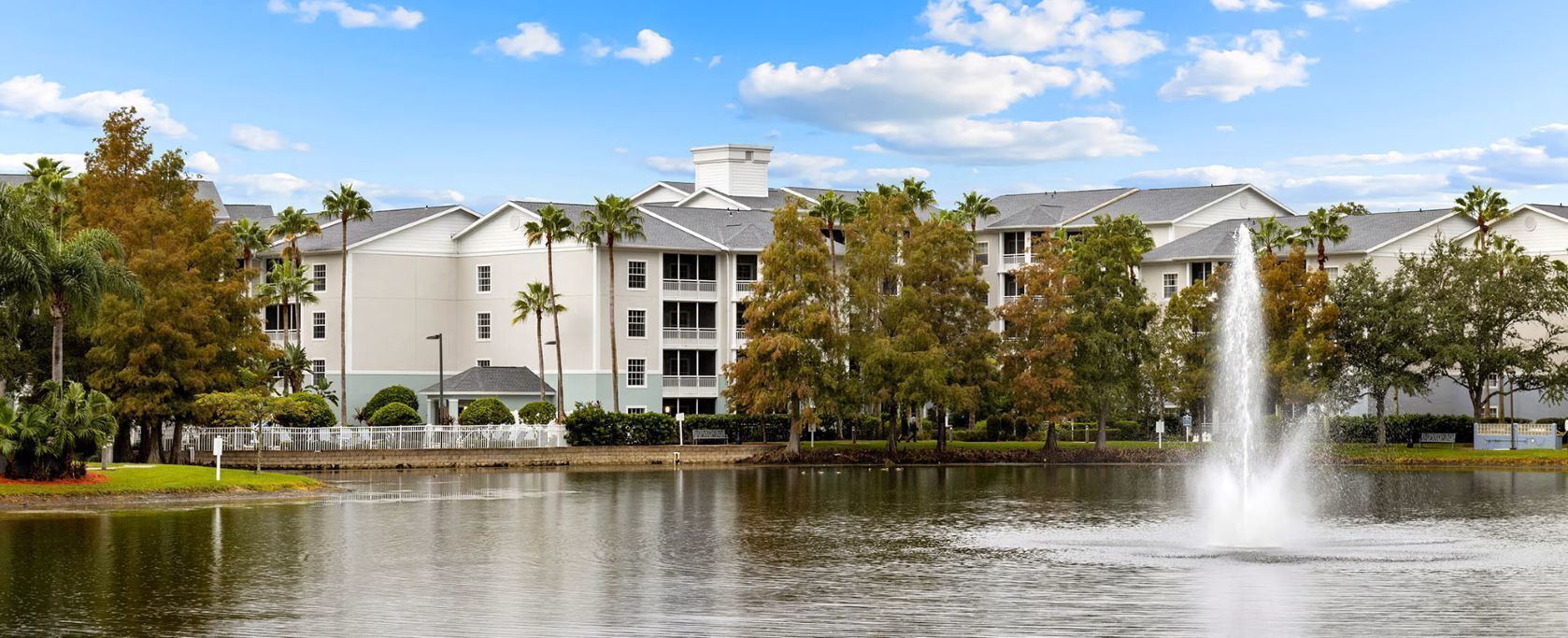 A hotel with a water fountain, surrounded by trees and a calm lake.