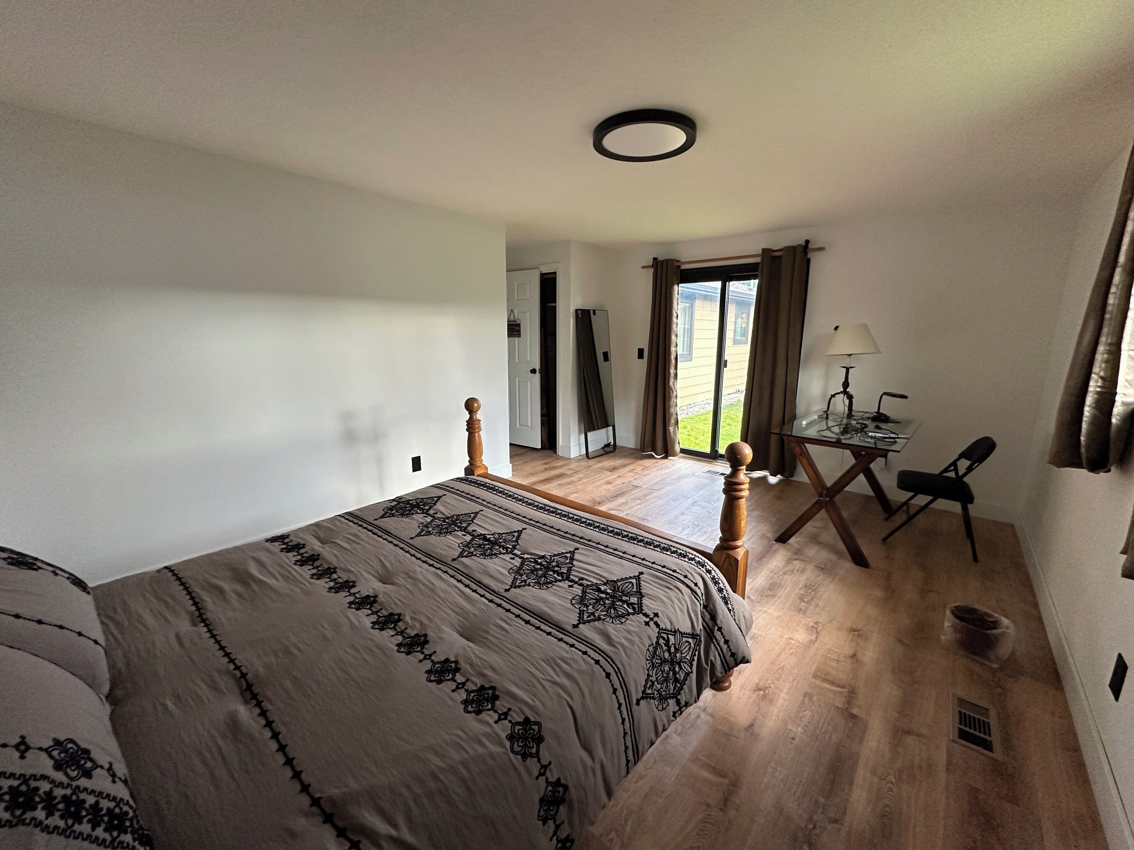 A bedroom with a bed, a desk, and a chair. There is a door leading to a balcony.