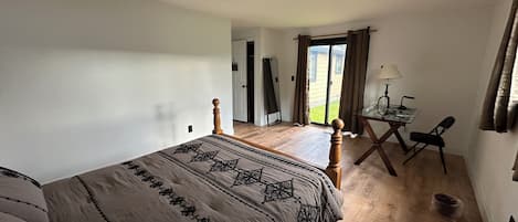 A bedroom with a bed, a desk, and a chair. There is a door leading to a balcony.