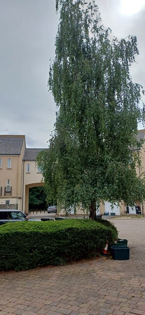 A tree-lined residential area with a paved walkway, a parked car, and a building with a flat roof. - Stylish yet Cosy 3-Bed Flat with Private Balcony. (Stoke Gifford)