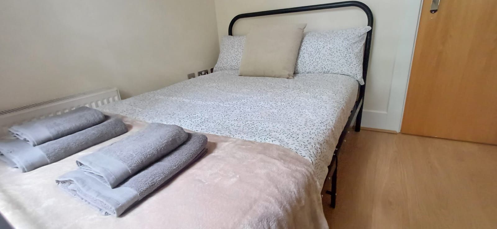 A single bed with a patterned bedspread, two pillows, and a folded blanket on the side.