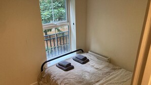 Una habitación pequeña con cama individual, ventana, radiador y suelo de madera.