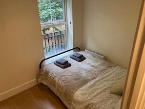 Ein kleines Zimmer mit Einzelbett, Fenster, Heizkörper und Holzboden.