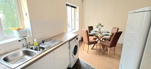 Cuina compacta amb rentadora, un rentaplat i zona de dinar amb cadires i taula per a quatre.