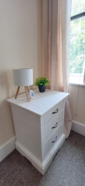 A white dresser with three drawers, a small lamp, and a potted plant. - Stylish yet Cosy 3-Bed Flat with Private Balcony. (Stoke Gifford)