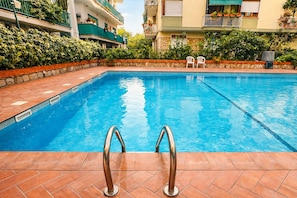 A swimming pool with a tiled deck, metal pool ladders, and a stone wall. - Sorrento Pool House: Spacious Family Apartment in the Center (Sorrento)