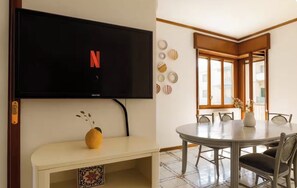 A living room with a flat-screen TV mounted on the wall, a round dining table with chairs, a small white cabinet with a vase, and decorative plates on the wall. - Sorrento Pool House: Spacious Family Apartment in the Center (Sorrento)