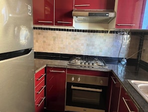A kitchen with red cabinets, a stainless steel refrigerator, a gas stove, and a tiled backsplash. - 2-bedroom apartment in enchanting Ouahat Sidi Brahim with AC (Ouahat Sidi Brahim)