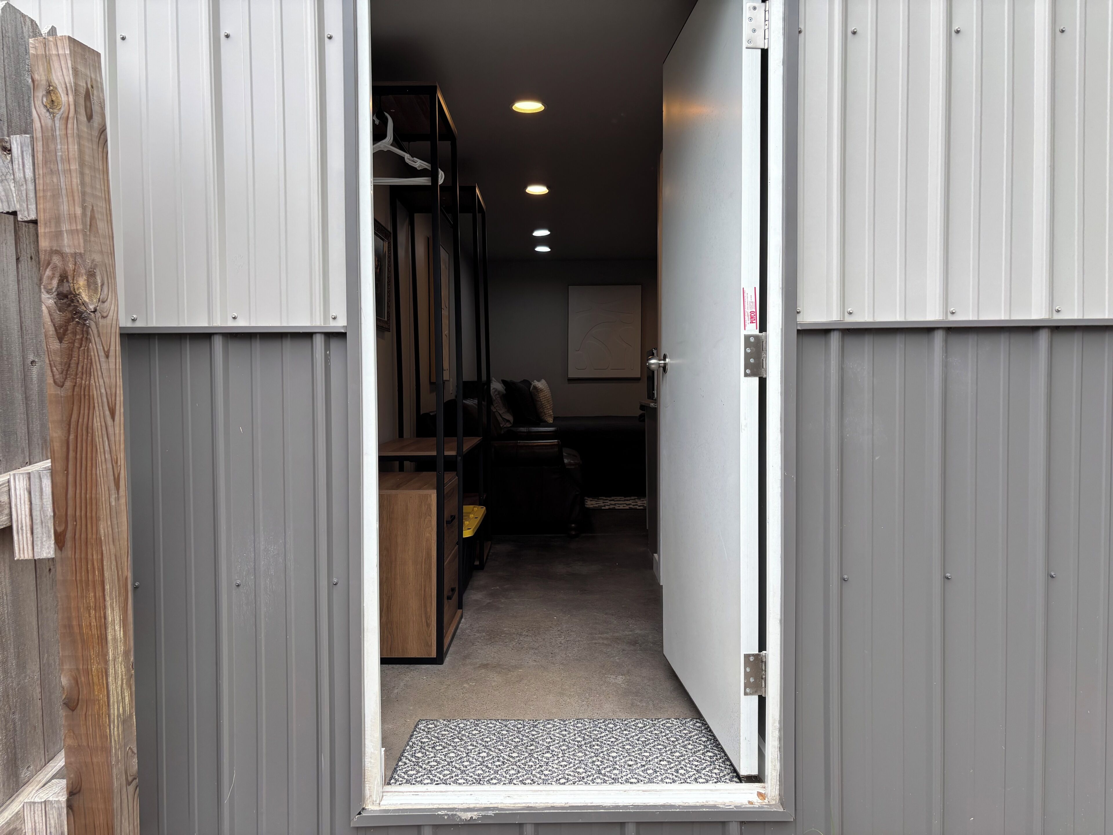 Un couloir étroit, avec un cadre de porte en bois, une porte en métal et un paillasson à l’entrée.
