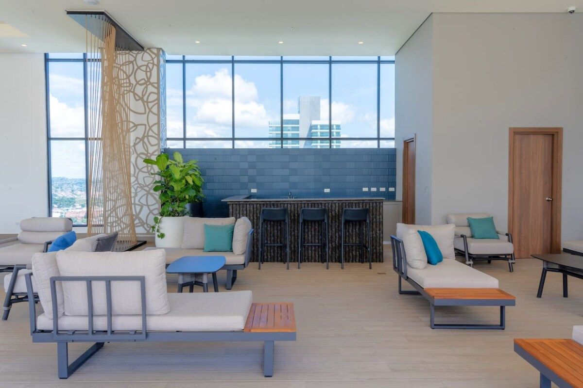 A modern lounge area with seating, a bar, and a large window offering a city view.