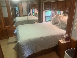 A bedroom with two beds, wooden cabinets, a window with curtains, and a bedside table with a tissue box. - Experience a unique stay in a well appointed motorhome (Willsboro)