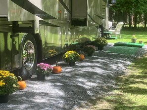 A green RV parked on a gravel driveway with potted plants and a lawn chair. - Experience a unique stay in a well appointed motorhome (Willsboro)
