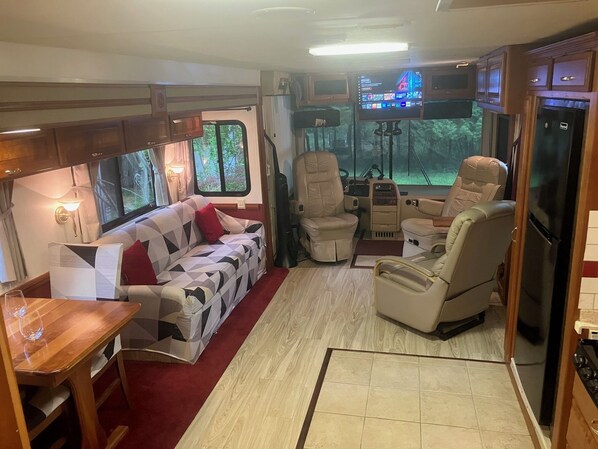 A cozy RV interior with a sofa, chairs, a dining table, and a kitchen area. - Experience a unique stay in a well appointed motorhome (Willsboro)