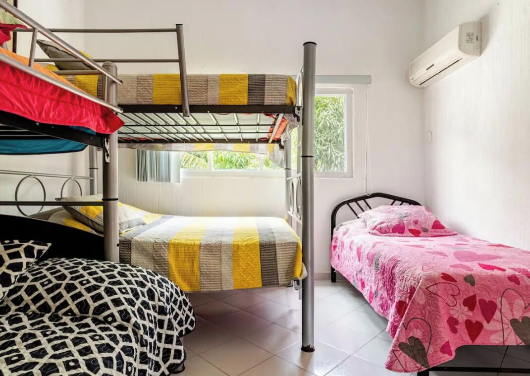 A dormitory room with bunk beds, a single bed, and a window with a view of greenery.