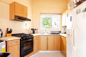 Cocina compacta con armarios de madera, estufa a gas, horno empotrado y refrigerador blanco.