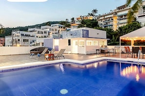Una piscina en la azotea con sillones de descanso, zona de comedor y vistas de edificios circundantes.