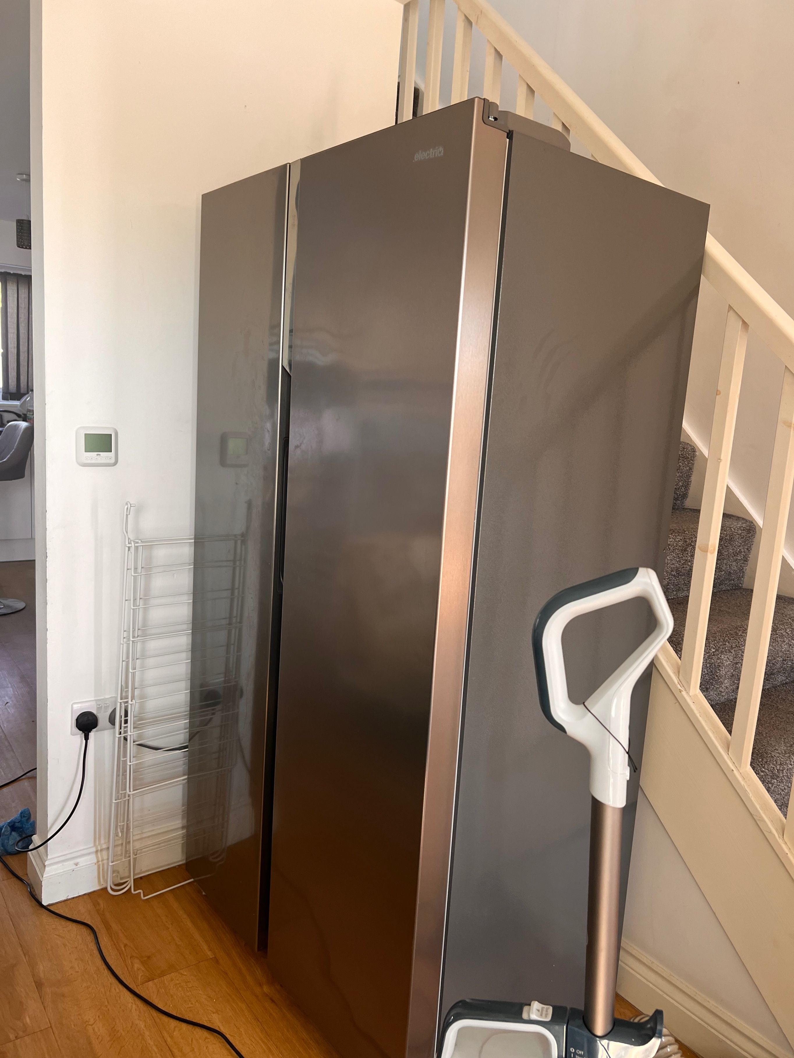 A stainless steel refrigerator with a control panel, a white power outlet, and a white object on the floor.