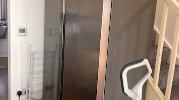 A stainless steel refrigerator with a control panel, a white power outlet, and a white object on the floor.