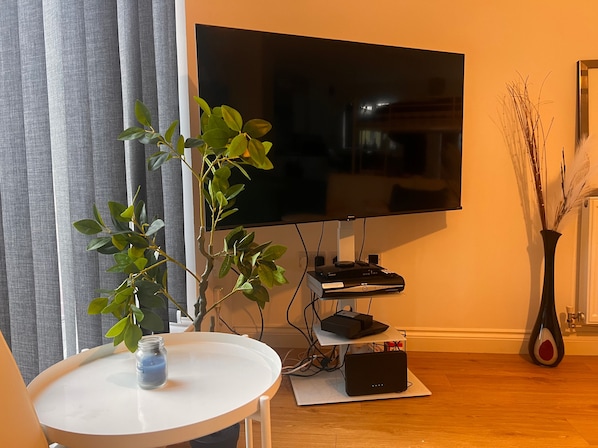 A living room with a flat-screen TV mounted on the wall, a small table with a vase, and a plant. - Cozy Crook Retreat With 2 Bedrooms Near Kyren (Crook)