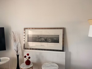 A framed cityscape photograph on a wall, a white radiator below, and a vase with red flowers on a small table. - Cozy Crook Retreat With 2 Bedrooms Near Kyren (Crook)