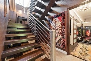 A wooden staircase with a metal handrail leading to a room with a patterned rug and a decorative wall hanging. - Cougar Cañon Ranch, Colorado Mountain Retreat - Incredible Views and Amenities (Cañon City)