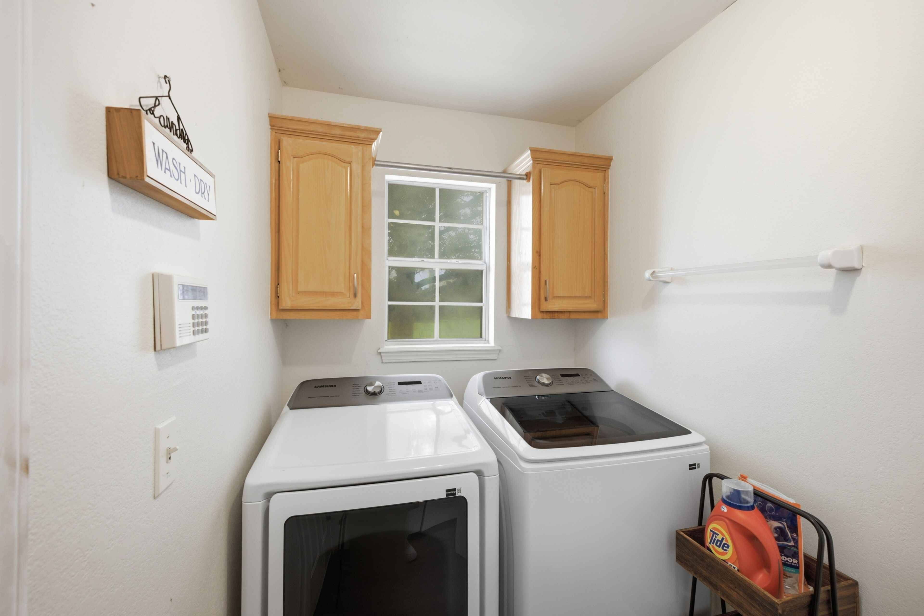 A laundry room with two washing machines, a window, wooden cabinets, and a wall-mounted laundry detergent dispenser.