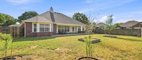 Un patio trasero residencial con una casa, patio cercado y zonas ajardinadas con árboles.