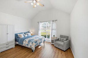 A bedroom with a bed, a nightstand, a chair, a window with blinds, and a ceiling fan.