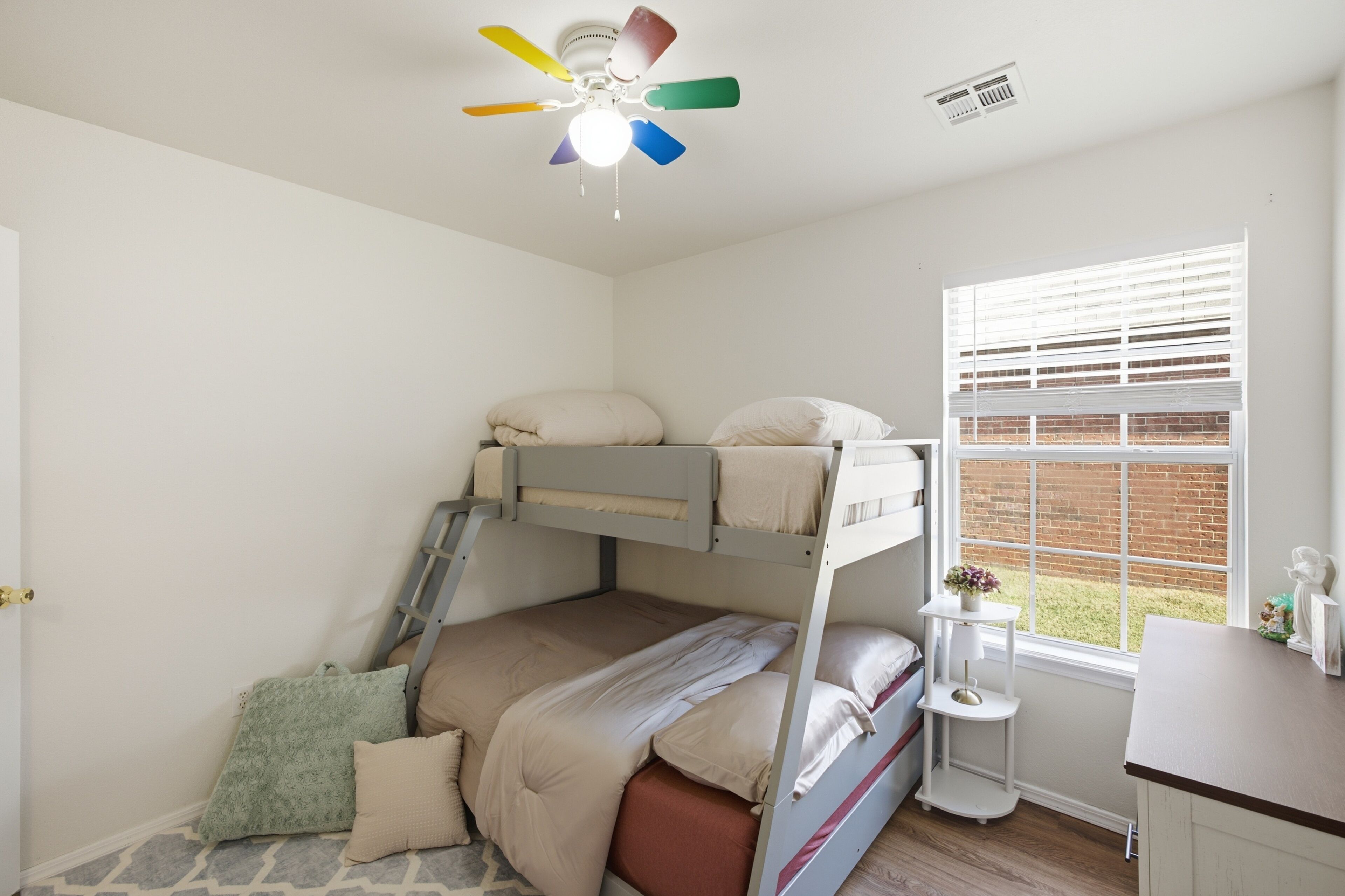 A bunk bed room with a ceiling fan, a window with blinds, and a small table with a plant.