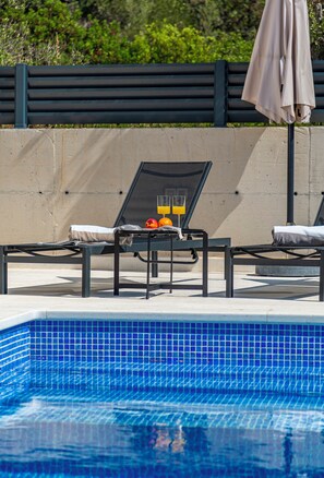 Ein Poolbereich mit Liegestühlen, einem Tisch mit Obst und Getränken sowie einer Betonwand.
