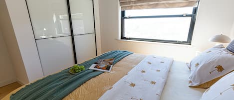 Un dormitorio con cama, ventana, mesita de noche y lámpara.