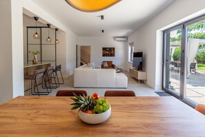 Ein modernes Interieur mit Essbereich, einer Couch, einem Fernseher und Blick ins Freie.