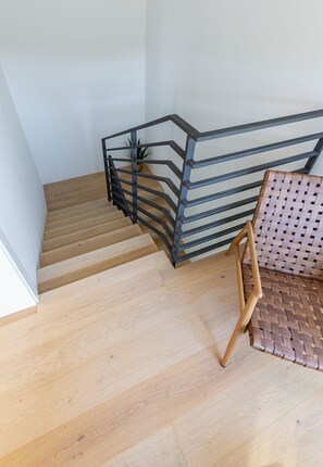 Eine Holztreppe mit Metallgeländer, ein gewebter Stuhl und ein Blumentopf.