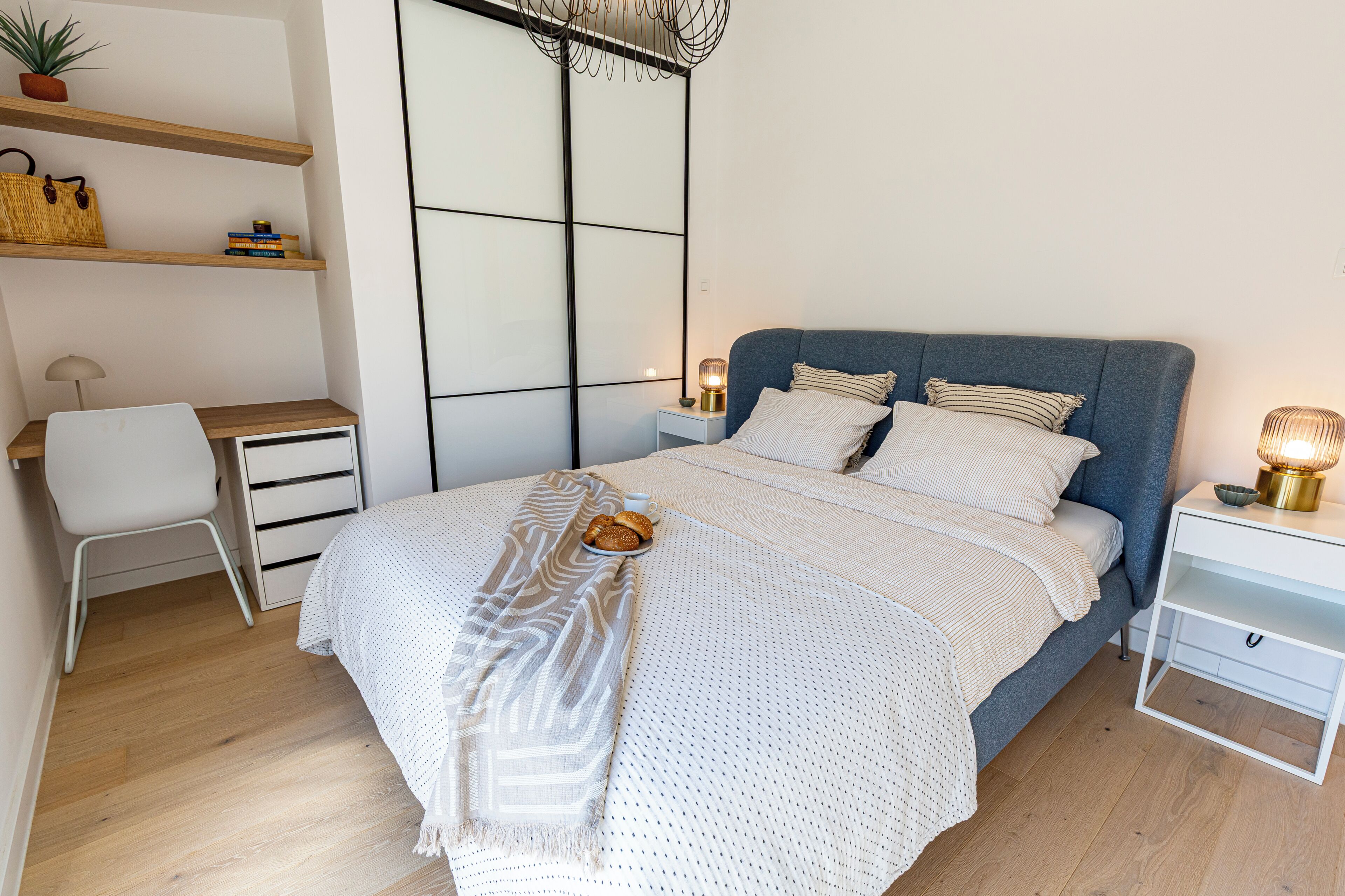A modern bedroom with a bed, bedside tables, a desk, and a chair.