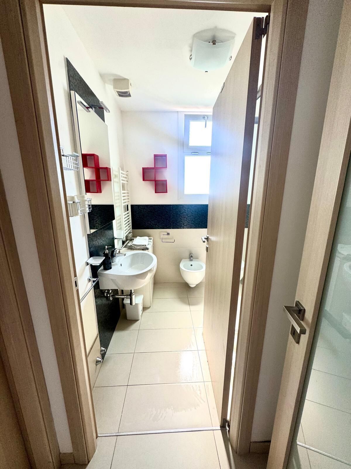 Ein schmaler Flur, der zu einem Badezimmer mit Waschbecken, Bidet und Spiegel führt.