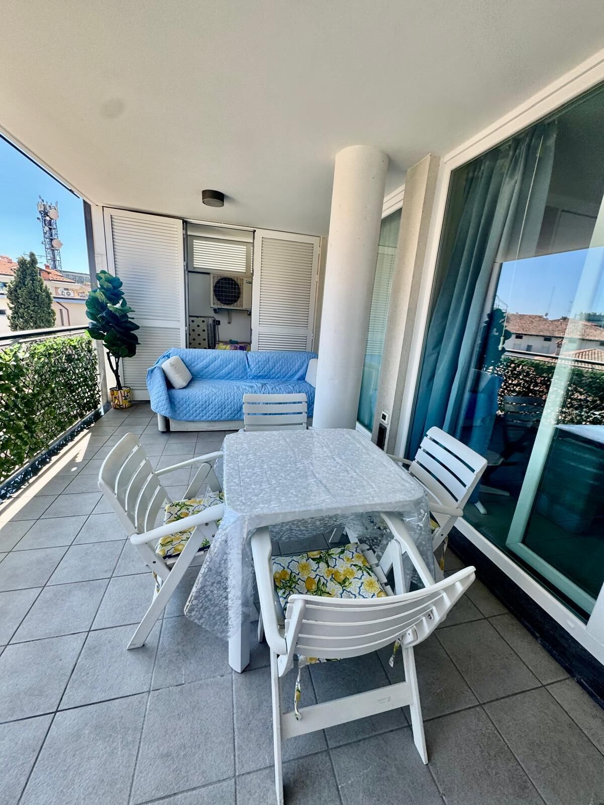 Un balcon avec une table et des chaises, un canapé bleu et une plante en pot.