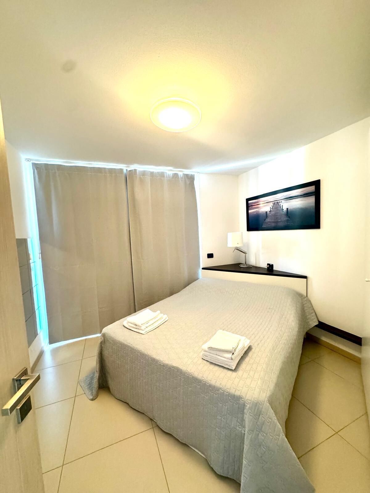 Ein Hotelzimmer mit Bett, Wandfernseher und Vorhängen am Fenster.