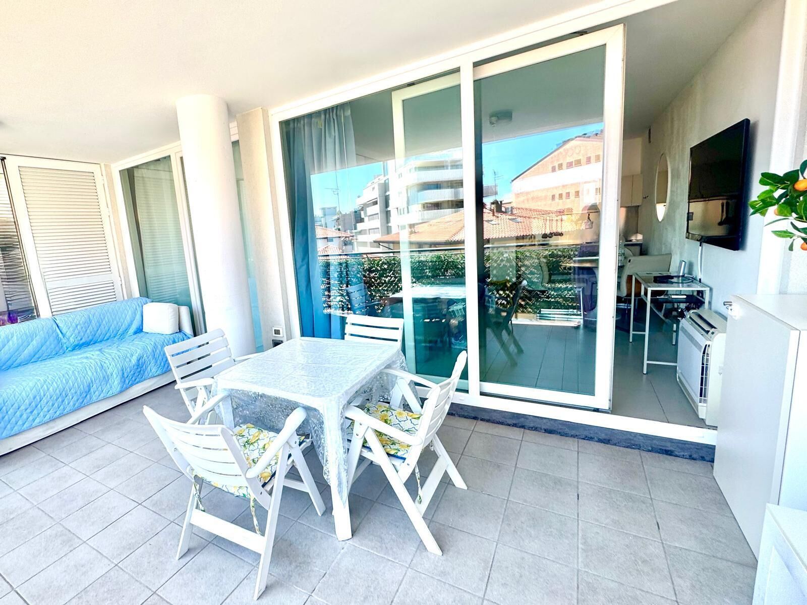 A balcony with a table and chairs, a sofa, a sliding glass door, and a television.