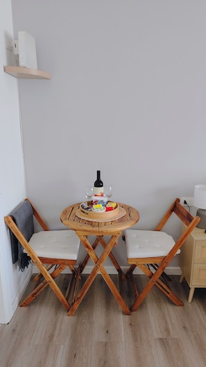Ett hörnrum med ett runt träbord, två hopfällbara stolar, en flaska vin och lite snacks.